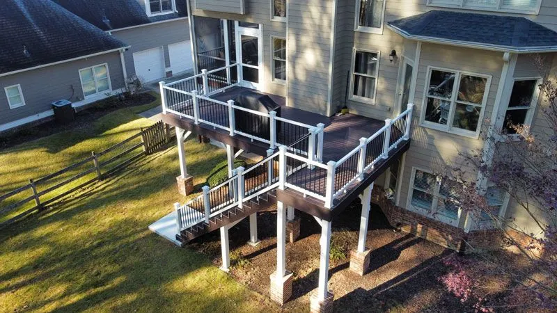 A high-angle view of a custom multi-level dark wood deck attached to a suburban home.