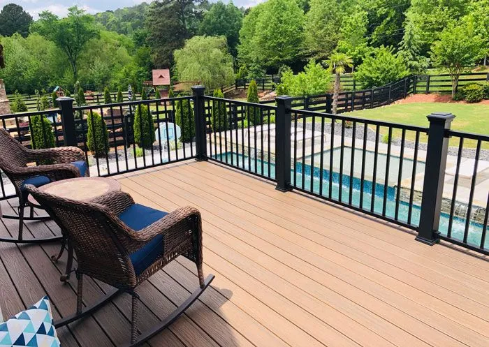 Modern tan composite deck with black metal railings overlooking a backyard swimming pool.