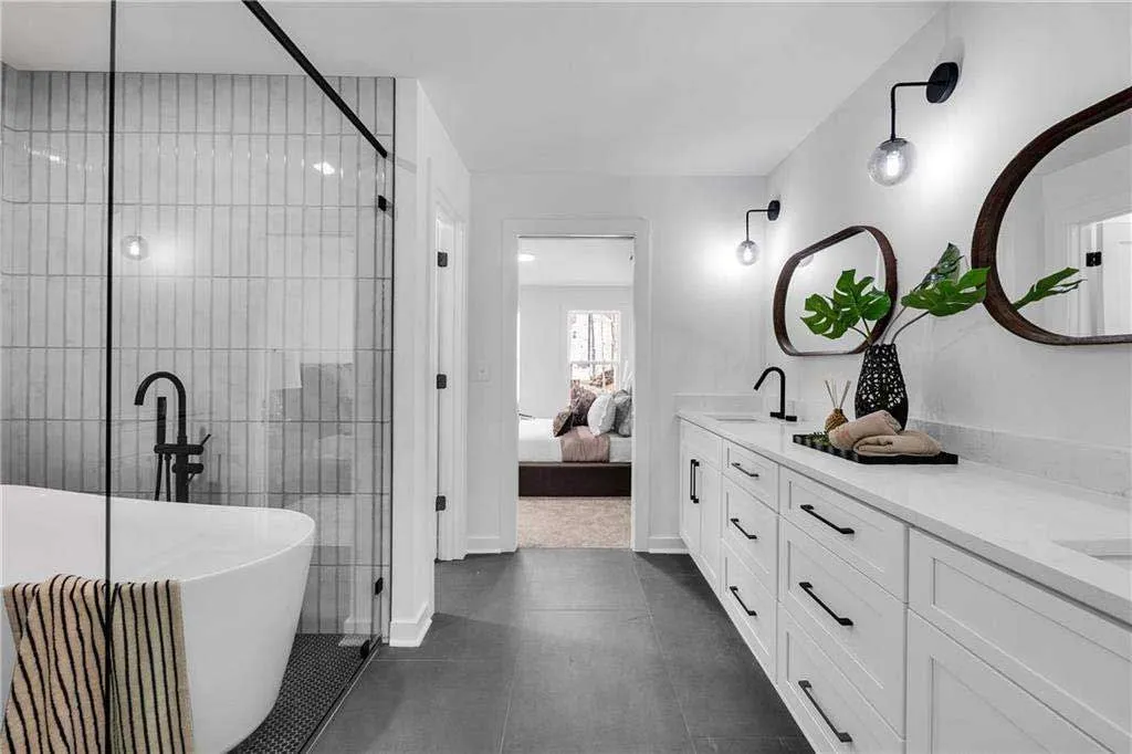 Bright modern bathroom featuring white cabinets, dark floors, and a soaking tub.