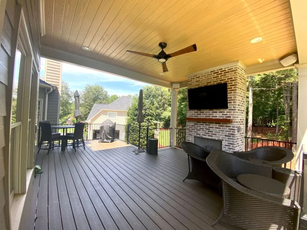 Large dark wood deck under a covered roof with a ceiling fan and stone fireplace.