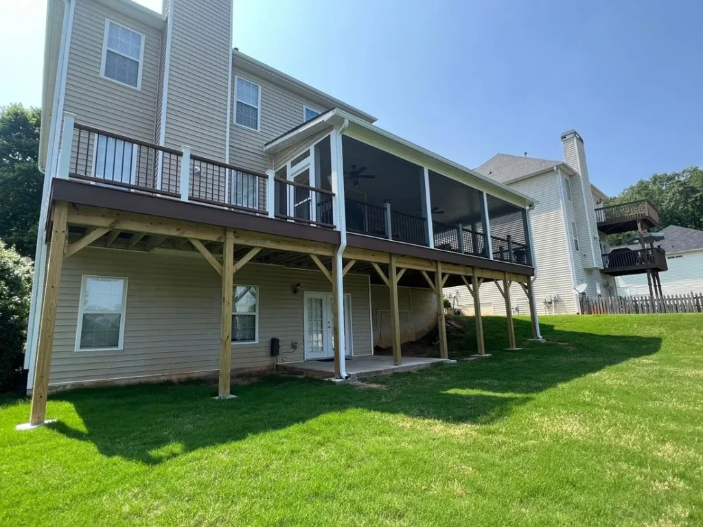 The rear exterior of a beige two-story house featuring a large elevated wooden deck and screened porch.