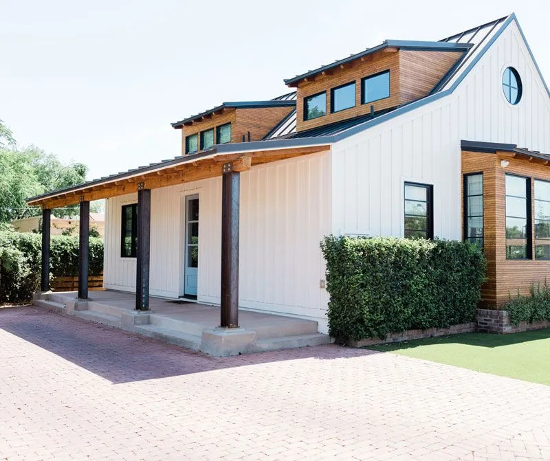 A modern ranch-style home featuring white vertical siding and a large covered porch.