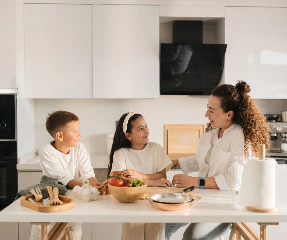 A mother and two children sitting at a white kitchen island preparing food.
