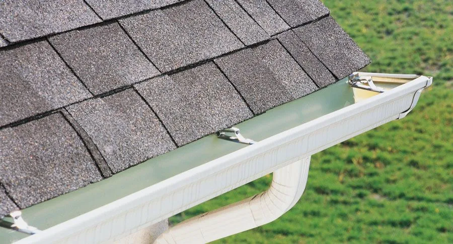 A white gutter with a micro-mesh leaf guard under shingle roof edges.