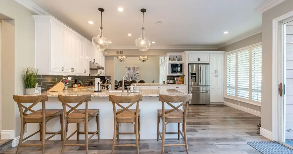 Bright kitchen with white cabinetry, granite countertops, and wooden barstools at the island.