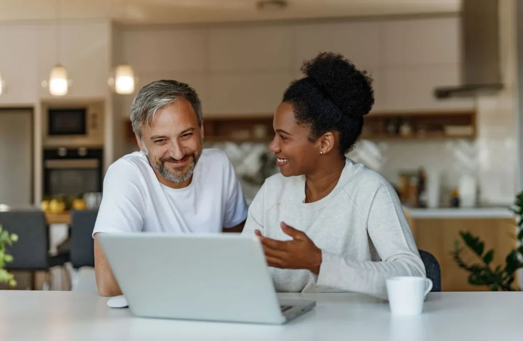 Smiling man and woman sitting at a table looking at a laptop together.