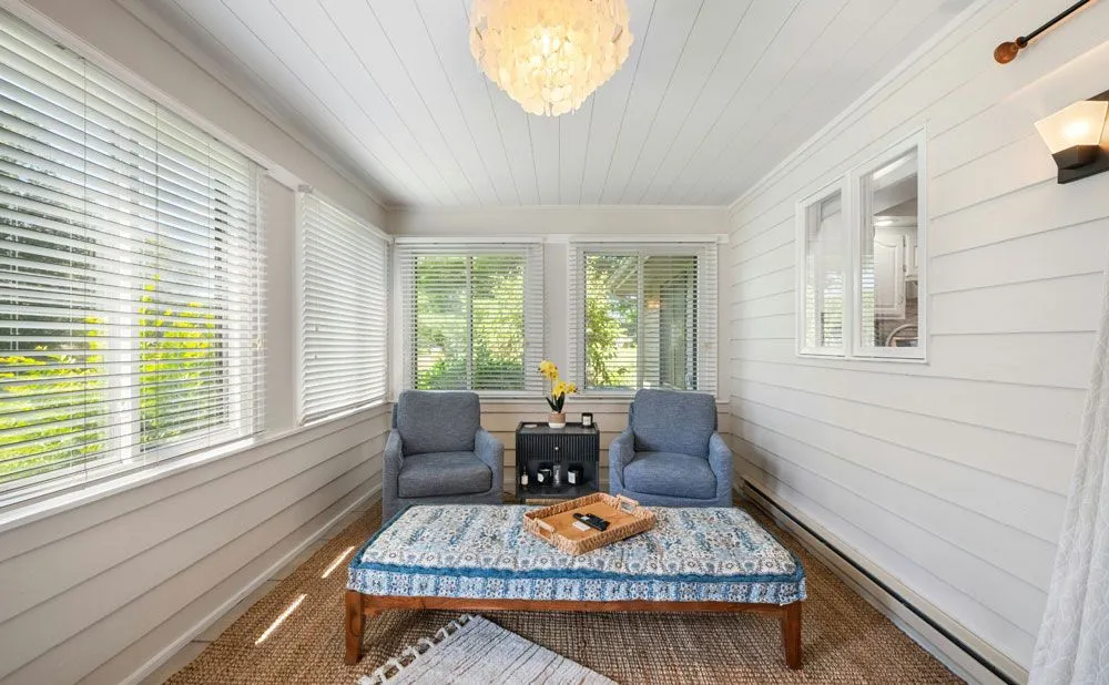 Bright sunroom with white shiplap walls, blue armchairs, and large windows with blinds.