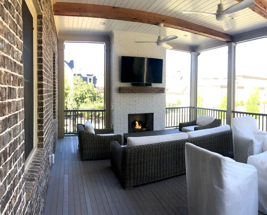 Modern covered porch featuring a stone fireplace, wall-mounted TV, and ceiling fan.