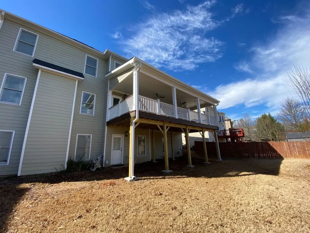 Large covered wooden deck attached to the rear of a multi-story house.