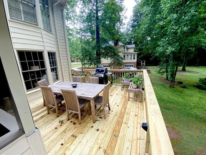 High-angle view of a large wooden deck featuring a dining table, chairs, and a grill.