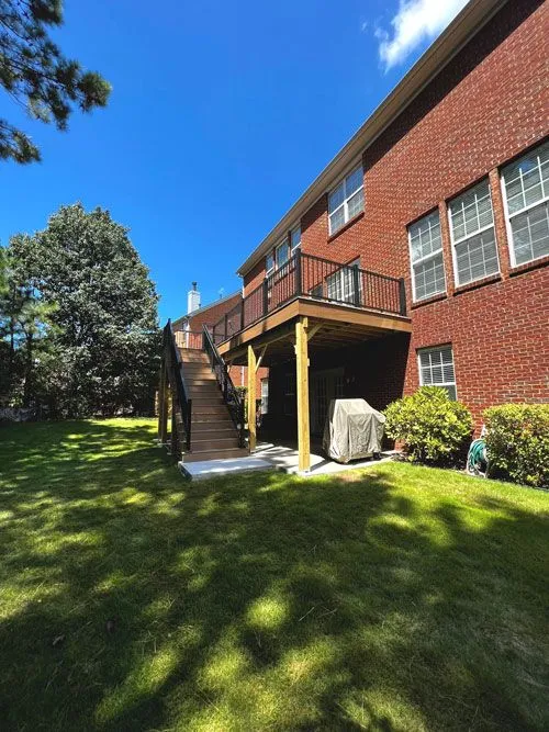 Newly built wooden deck with black railings attached to a two-story red brick house.