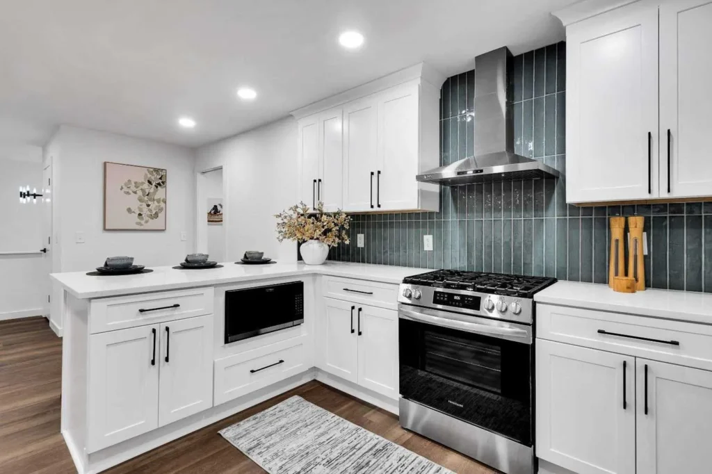 Modern white kitchen featuring a gas range, stainless steel hood, and blue tiled backsplash.