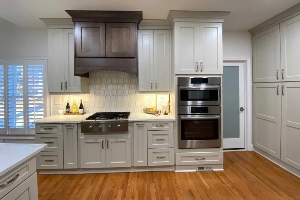 White kitchen cabinets with a dark wood custom vent hood and gas range.