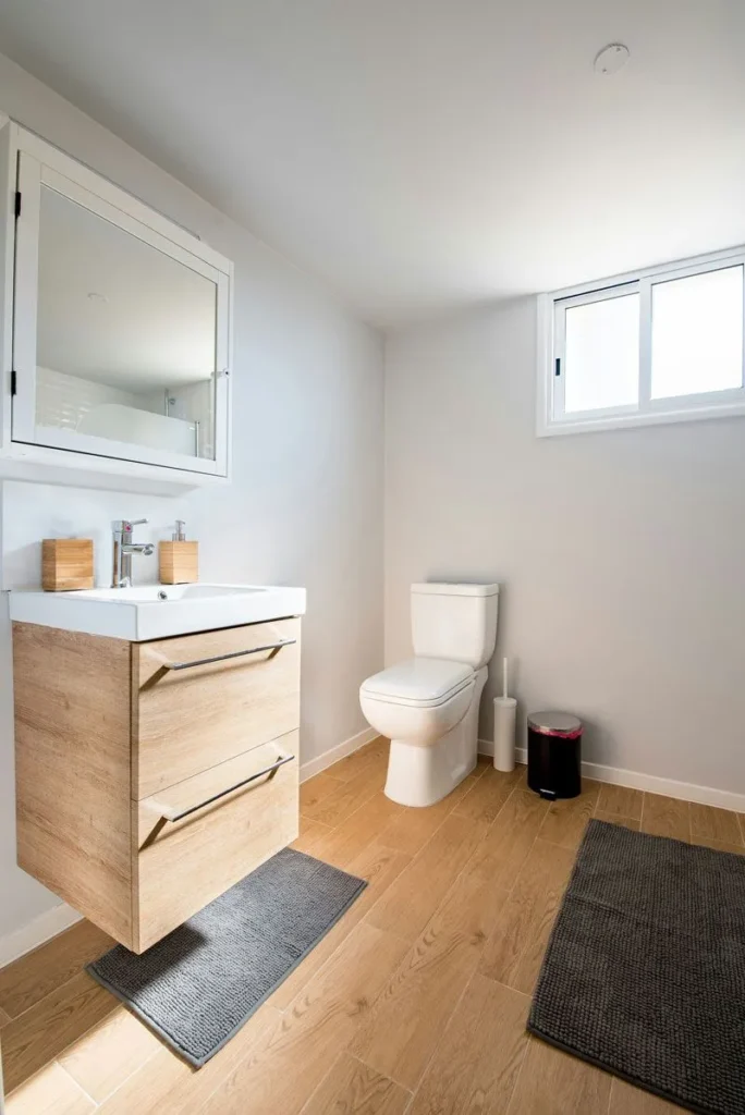Modern bathroom with a floating wood vanity, white toilet, and oak flooring.