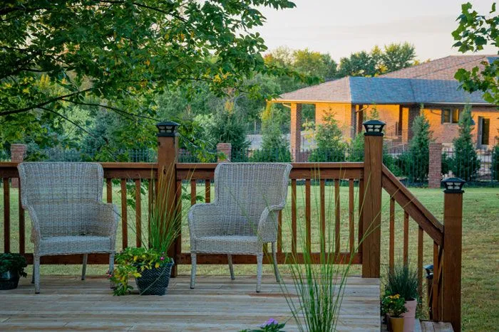 Spacious wooden backyard deck with comfortable wicker chairs overlooking a lawn.