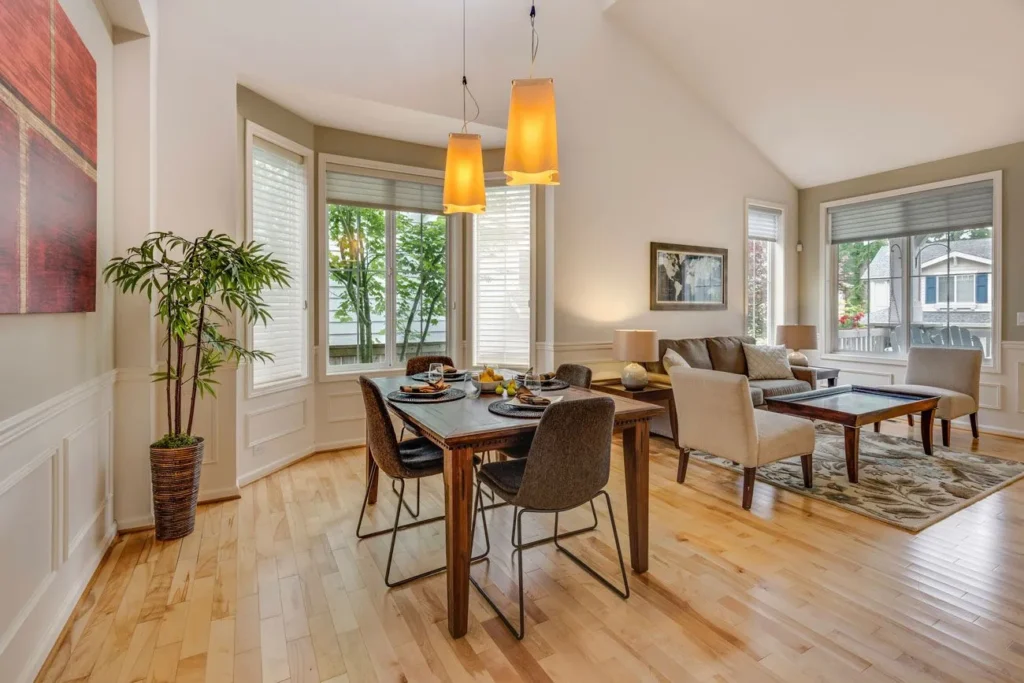 Modern dining table with black chairs adjacent to a bright living room.