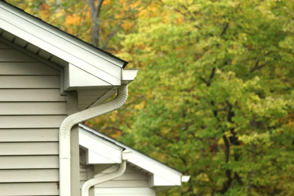 Clean white gutter downspout secured to beige lap siding on a house.