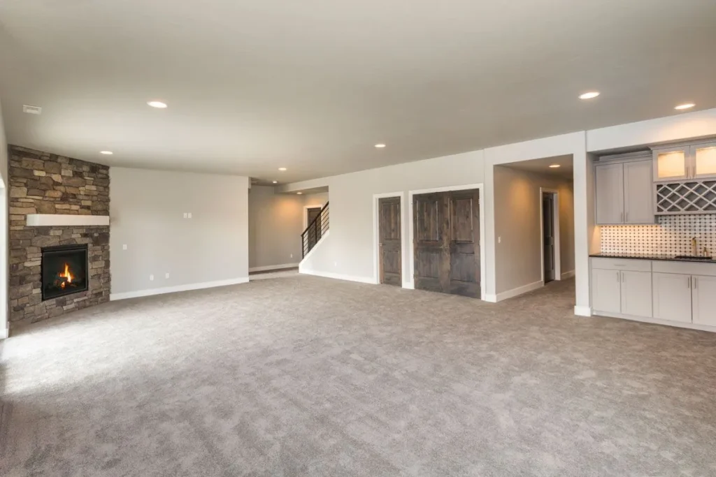Large empty basement area with support pillars and neutral carpeting.