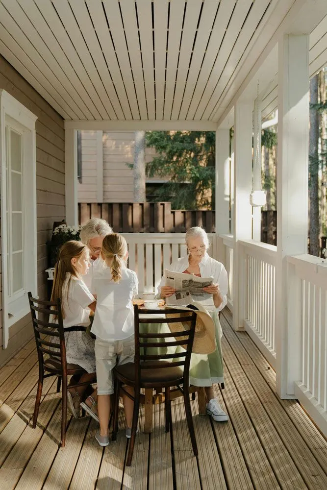 A family sitting at a wooden table on a white-railed porch during the daytime.