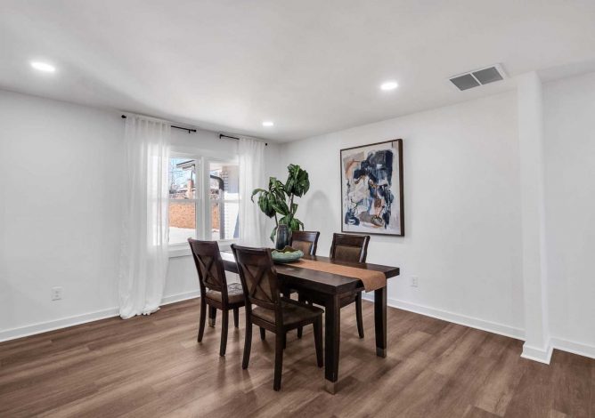 Dark wood dining table and chairs in a bright white room with large windows.