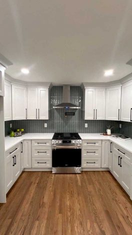 U-shaped kitchen with white cabinets, blue backsplash, and medium-tone wood floors.